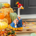 Decorative goose in overalls and hat surrounded by pumpkins and fall leaves