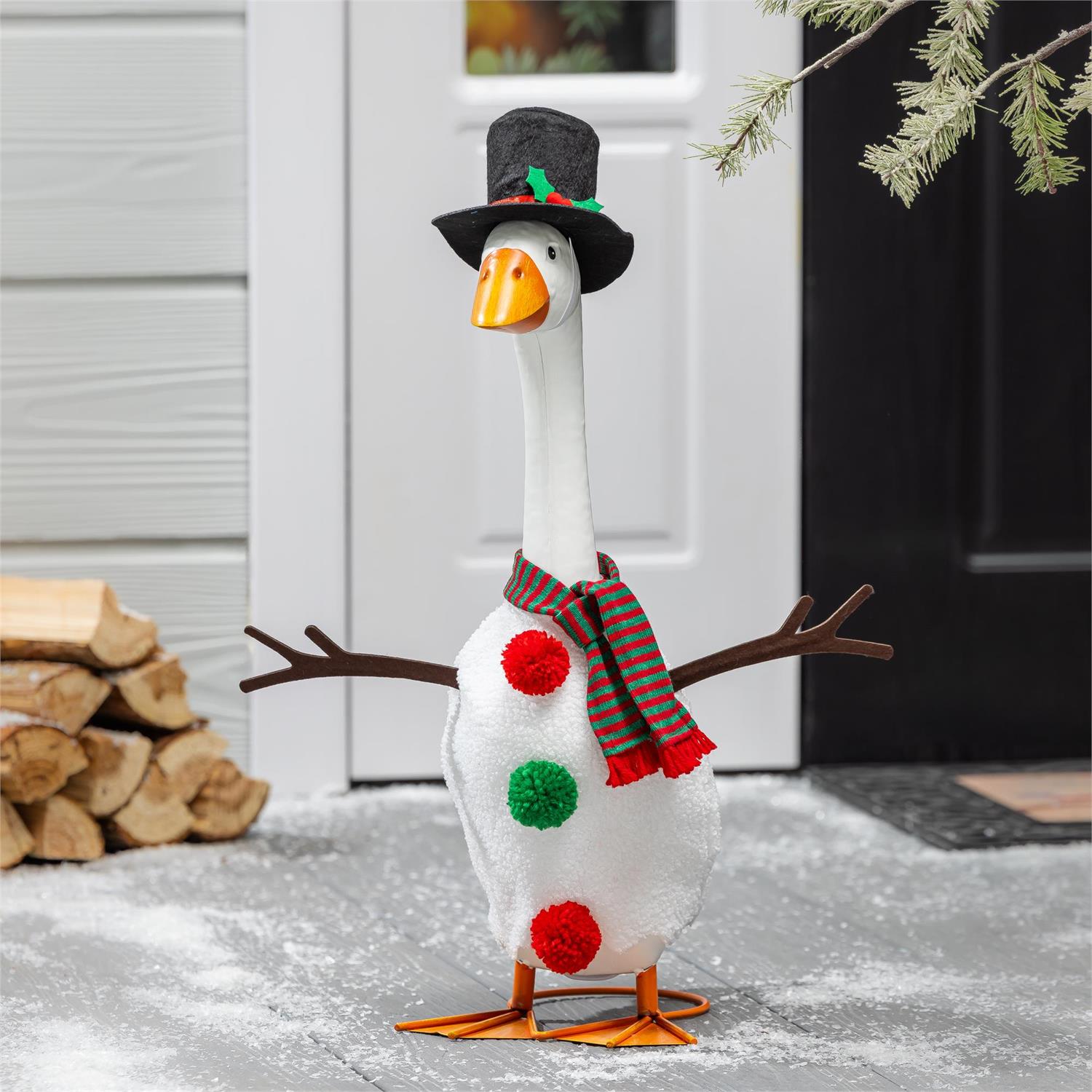 Decorative goose with a top hat, scarf, and pom-poms standing on a snowy ground.