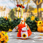 Giddy the Goose wearing a sunflower dress with matching hat and sunflower bag, displayed in a festive fall setting with pumpkins and autumn décor.
