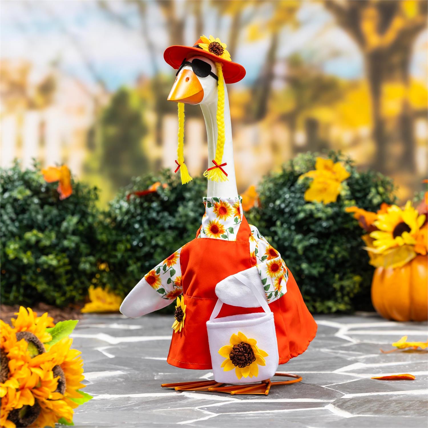 Giddy the Goose wearing a sunflower dress with matching hat and sunflower bag, displayed in a festive fall setting with pumpkins and autumn décor.
