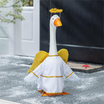 A white goose decoration dressed as an angel with yellow wings, a yellow halo, and gold trim, standing on a gray porch floor with snow-like dust.