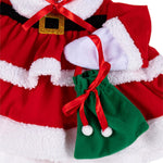 A close-up of a Christmas-themed pet outfit featuring a red and white faux-fur-trimmed dress with a black belt and gold buckle detail, plus a small green drawstring pouch with white pom-poms and a red ribbon.