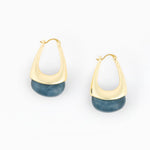 A pair of gold huggie hoop earrings with a semi-circular gold band and a polished blue stone drop at the bottom, shown on a clean white background.