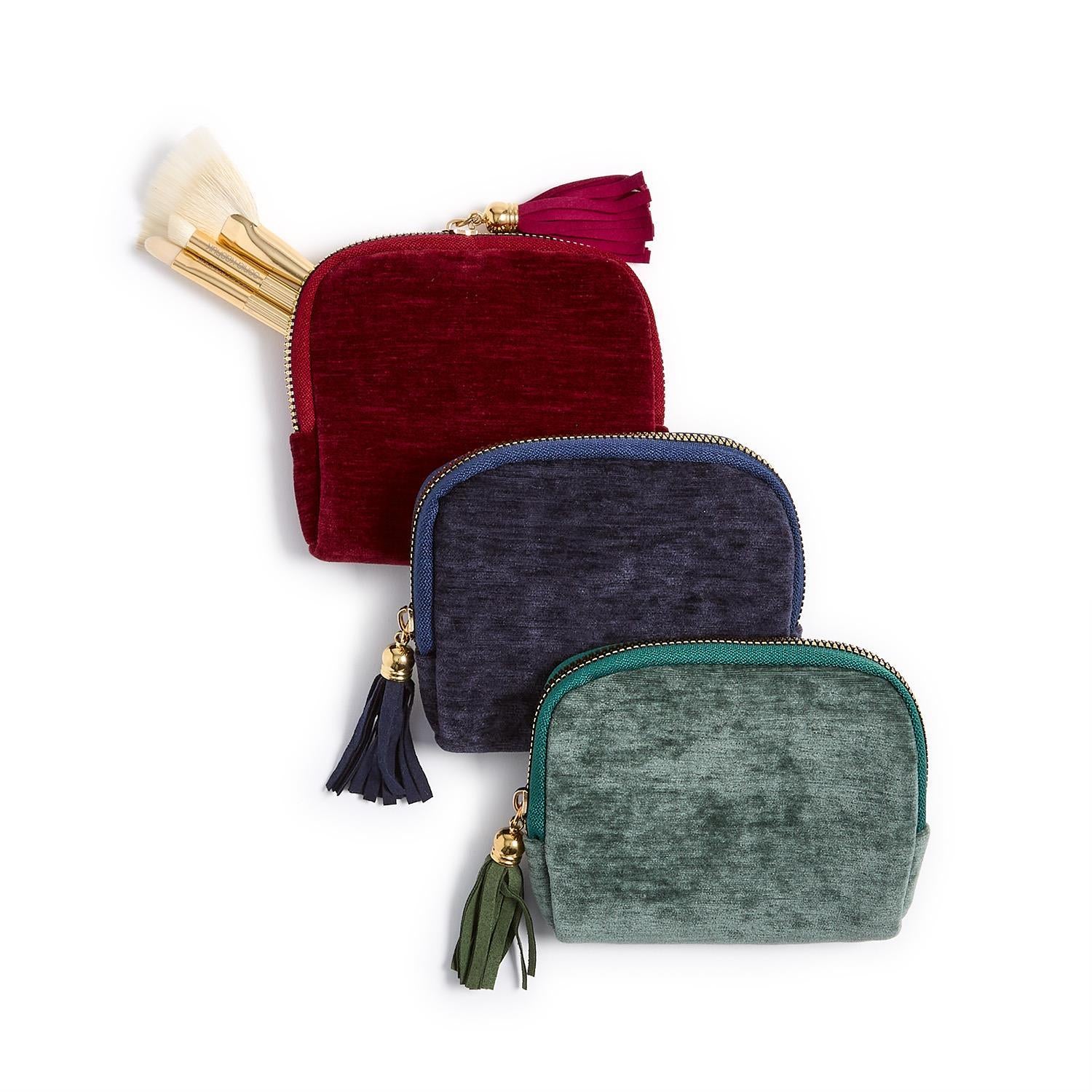 Three small velvet pouches in red, blue, and green with tassels on a white background