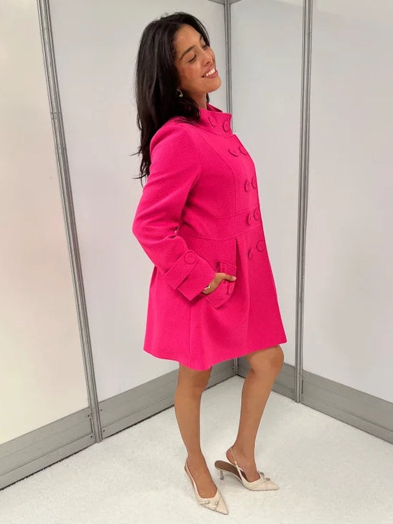 Women's hot pink honeycomb-textured statement coat with double-breasted covered buttons, high neckline, long sleeves, and front pockets.