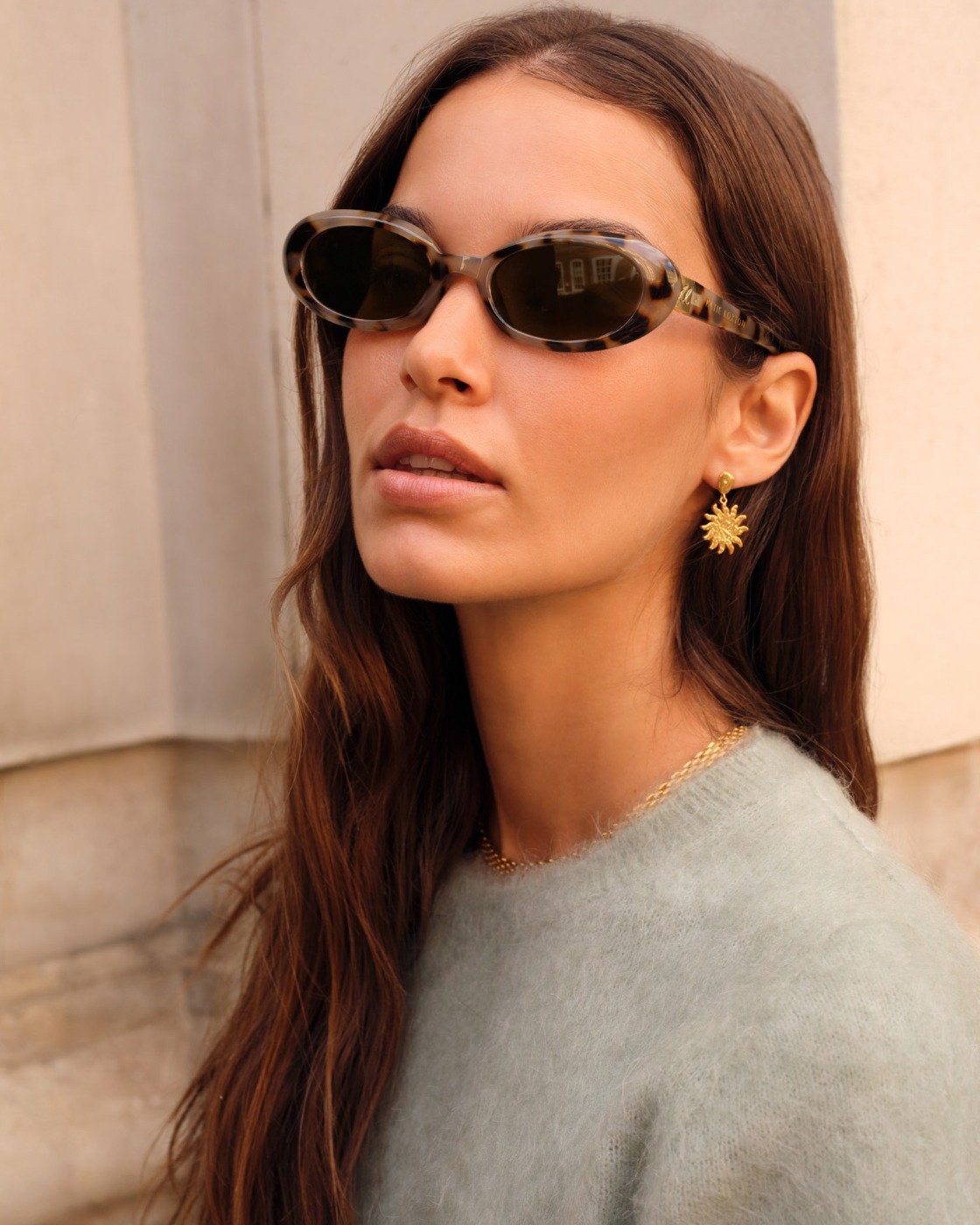 Woman wearing sunglasses and a light gray sweater with a neutral background