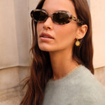 Woman wearing sunglasses and a light gray sweater with a neutral background