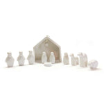 A miniature nativity set made of white porcelain, including figures representing the nativity scene and a white house, presented against a white background.